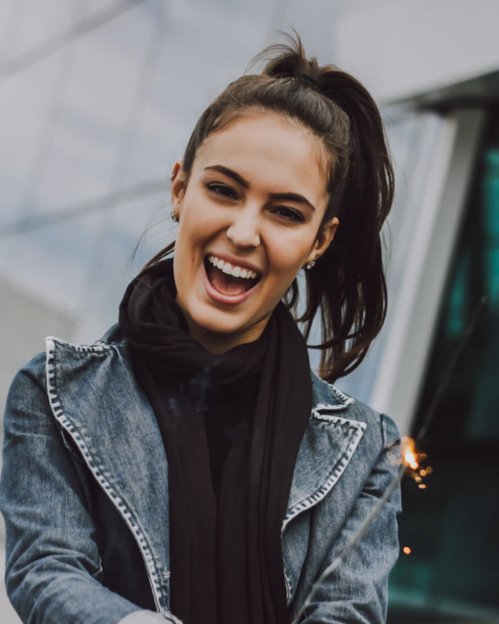 Mulher de cabelo comprido preso, rindo abertamente, de jaqueta jeans